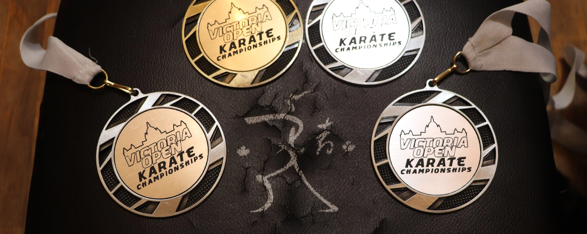 3 silver and 1 gold medal from Victoria Open Karate Tournament (2022) on a black impact pad with Shukokai written in white letters under a stick figure